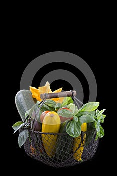 Fresh garden vegetables on iron basket on black