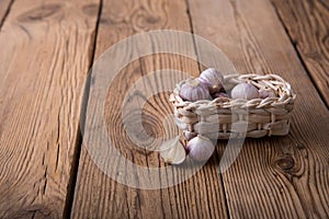 Fresh garlic in a craft wicker basket from a vine lies on an old wooden rustic table