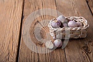 Fresh garlic in a craft wicker basket from a vine lies on an old wooden rustic table