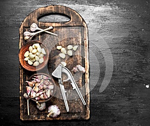 Fresh garlic with a press tool on a wooden board.