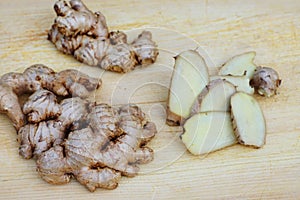 Fresh ginger root and ginger sliced on green leaf background on wood table background, healthy Asian herb concept