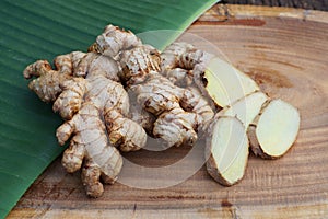 Fresh ginger root and ginger sliced on green leaf background on wood table background, healthy Asian herb concept