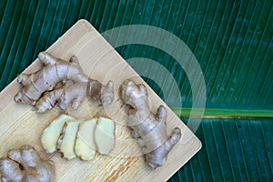 Fresh ginger root and ginger sliced on green leaf background on wood table background, healthy Asian herb concept