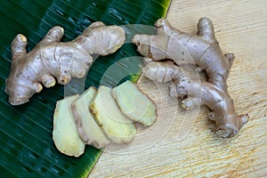 Fresh ginger root and ginger sliced on green leaf background on wood table background, healthy Asian herb concept