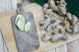 Fresh ginger root and ginger sliced on green leaf background on wood table background, healthy Asian herb concept