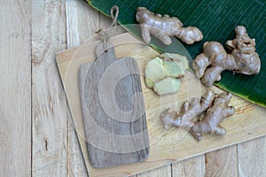 Fresh ginger root and ginger sliced on green leaf background on wood table background, healthy Asian herb concept