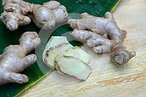 Fresh ginger root and ginger sliced on green leaf background on wood table background, healthy Asian herb concept