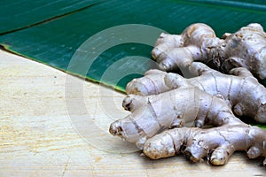 Fresh ginger root and ginger sliced on green leaf background on wood table background, healthy Asian herb concept