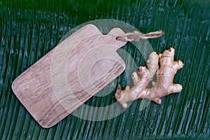 Fresh ginger root and ginger sliced on green leaf background on wood table background, healthy Asian herb concept