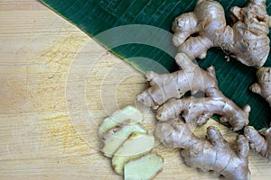 Fresh ginger root and ginger sliced on green leaf background on wood table background, healthy Asian herb concept