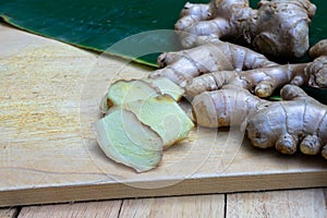 Fresh ginger root and ginger sliced on green leaf background on wood table background, healthy Asian herb concept