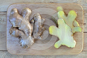 Fresh ginger root and ginger sliced on green leaf background on wood table background, healthy Asian herb concept