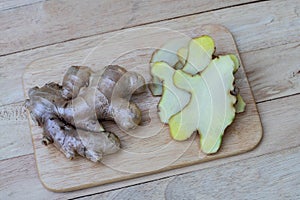 Fresh ginger root and ginger sliced on green leaf background on wood table background, healthy Asian herb concept