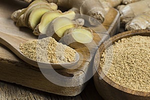 Fresh ginger root and ground ginger powder in wooden spoon on wooden rustic table photo