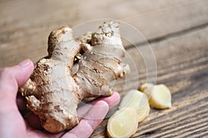 Fresh ginger root on hand with sliced ginger on wooden background