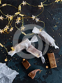 Fresh gold caramel toffee candies in white paper on blue dark background with garland in the form of luminous stars