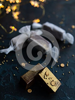 Fresh gold caramel toffee candies in white paper on blue dark background with garland in the form of luminous stars. Christmas,New