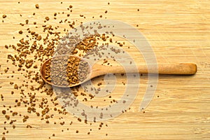 Fresh granules of instant coffee grains, in wooden spoon, on wooden background