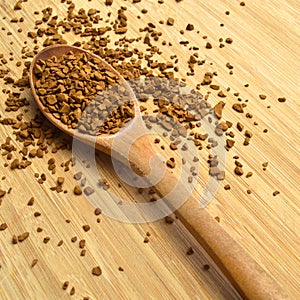 Fresh granules of instant coffee grains, in wooden spoon, on wooden background