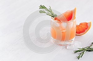 Fresh grapefruit juice with ice, piece and green rosemary on soft white wood table background.