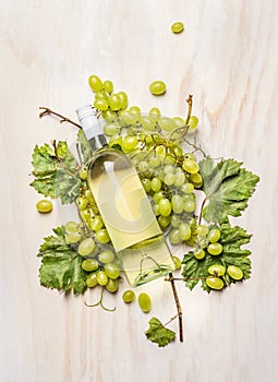 Fresh grapes on branch with leaves and bottle of white wine on white wooden background, top view