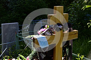 Fresh grave in the cemetery. On a simple wooden cross lies a disposable medical mask. Total quarantine from coronavirus in the Per