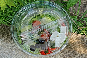 Fresh greek salad food in a transparent bowl with sunflower oil and a plastic white fork