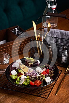 Fresh greek salad with tomato, radish, onion, bel pepper , olives and feta cheese on black plate, side view, wooden background