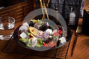 Fresh greek salad with tomato, radish, onion, bel pepper , olives and feta cheese on black plate, side view, wooden background