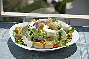 Fresh Greek salad on a white plate in the sun