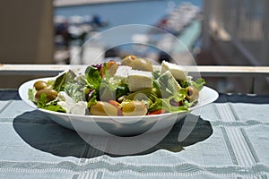 Fresh Greek salad on a white plate in the sun