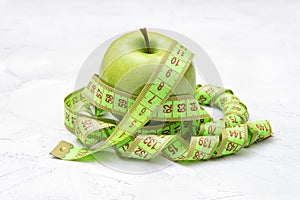 Fresh green apple with a measuring tape on a concrete table. Diet and weight loss concept