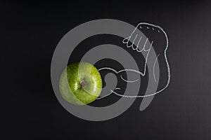 Fresh green apple and a strong arm showing its biceps muscle drawn in the black background