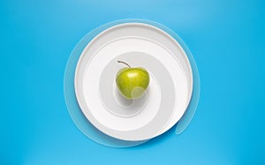 Fresh green apple on a white plate on a blue background