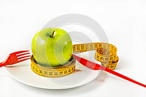 Fresh green apple with a yellow tape measure on a plate. Weight loss concept