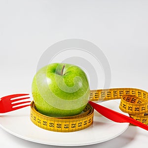 Fresh green apple with a yellow tape measure on a plate. Weight loss concept