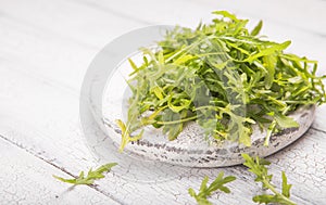 Fresh green arugula leaves on white board, rucola rocket salad on wooden rustic background with place for text. Selective focus,