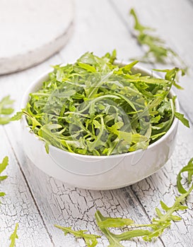 Fresh green arugula leaves on white bowl, rucola rocket salad on wooden rustic background with place for text. Selective focus,