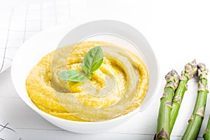 Fresh green asparagus cream soup on white wooden background