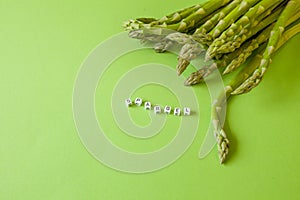 Fresh green asparagus on green background with copy space and cube letters