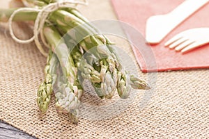 Fresh green asparagus on old kitchen table and with an eco-friendly wooden knife and fork on a red napkin.