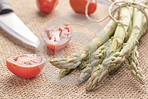 Fresh green asparagus on an old kitchen table with a knife and cherry tomatoes