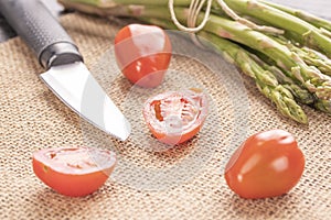 Fresh green asparagus on an old kitchen table with a knife and cherry tomatoes