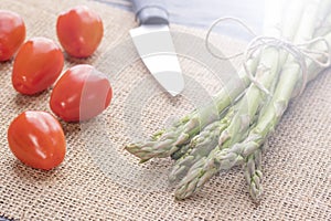 Fresh green asparagus on an old kitchen table with a knife and cherry tomatoes