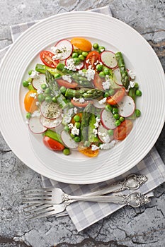 Fresh Green Asparagus salad witch goat cheese, green peas, radish and tomato closeup on the plate. Vertical top view