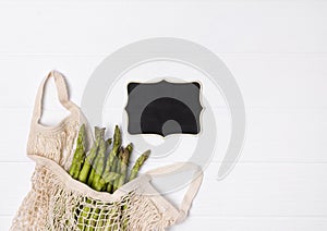 Fresh green asparagus in string shopping bag on white wooden table background