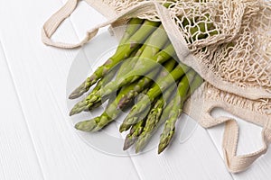 Fresh green asparagus in string shopping bag on white wooden table background