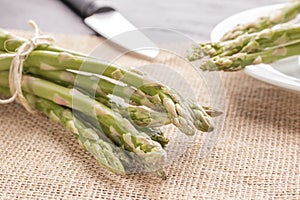 Fresh green asparagus on the table and in a white plate with a shiny knife