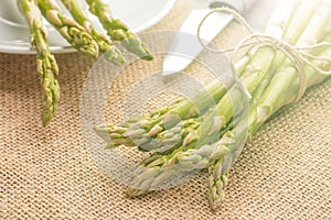 Fresh green asparagus on the table and in a white plate with a shiny knife