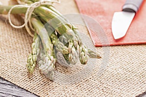 Fresh green asparagus on a table and in a white plate, tied with a rope, with a knife on a red napkin